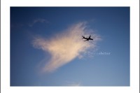 An airplane flies past an airplane shaped cloud.